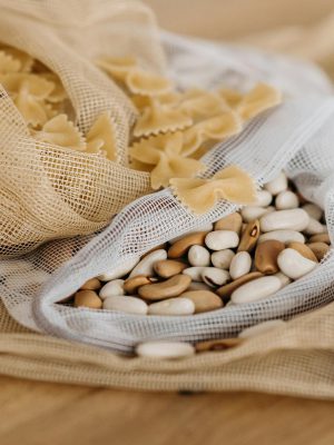 Eco-friendly bags filled with raw farfalle pasta and mixed beans on a wooden surface.